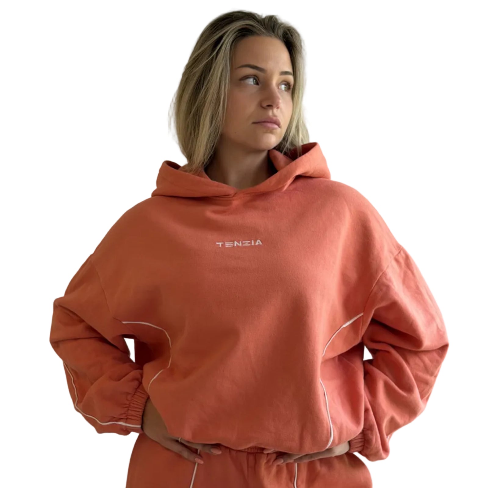 Person wearing a coral tracksuit with 'TENZIA' branding against a plain background