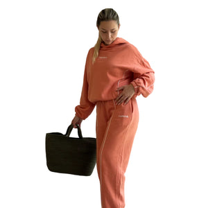 Person wearing a matching peach tracksuit holding a black bag indoors.