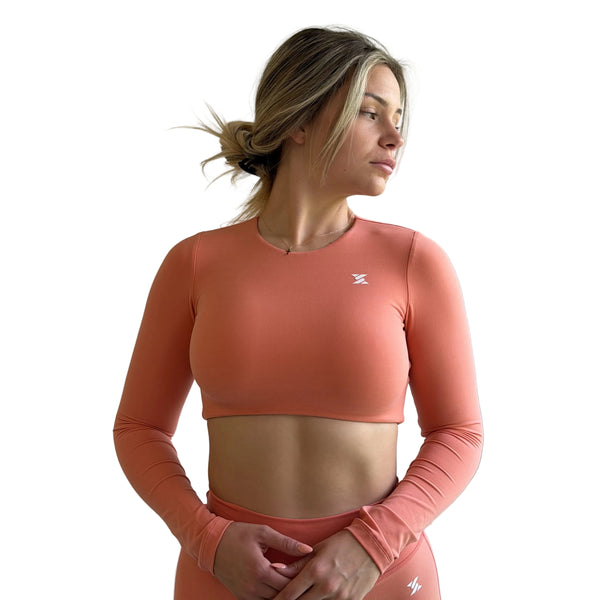 Woman wearing a coral long-sleeve athletic top and shorts against a neutral background